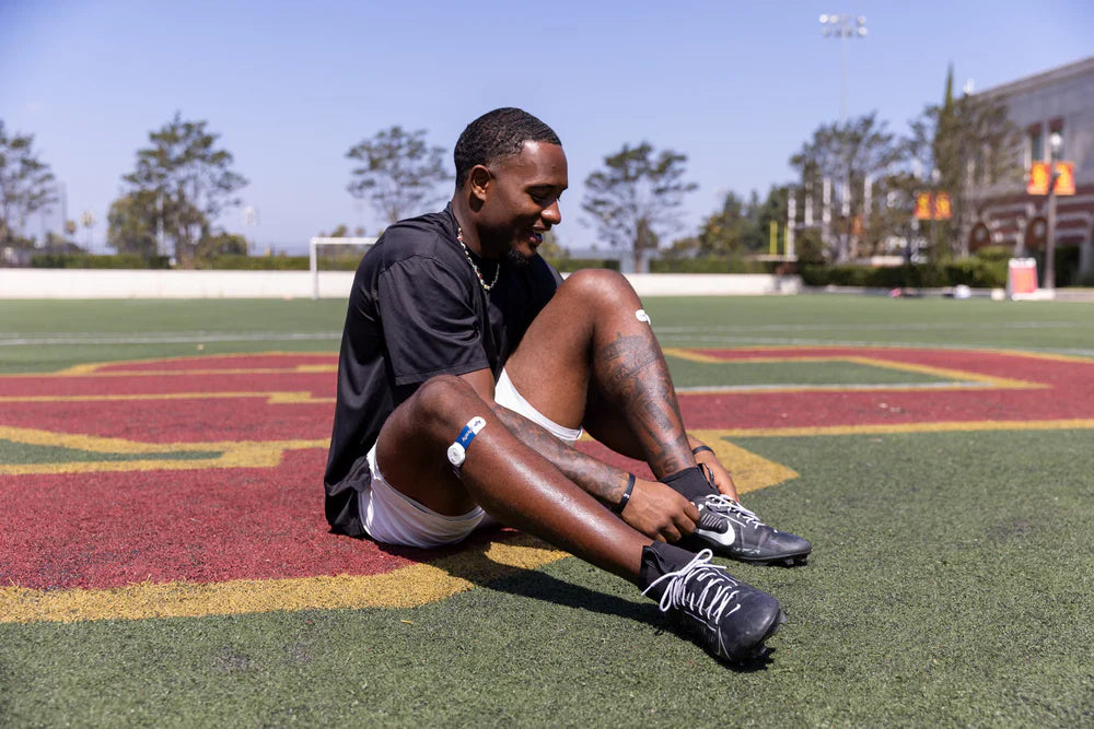 Athlete resting on ground post-workout, using Firefly on legs to boost circulation and improve performance.